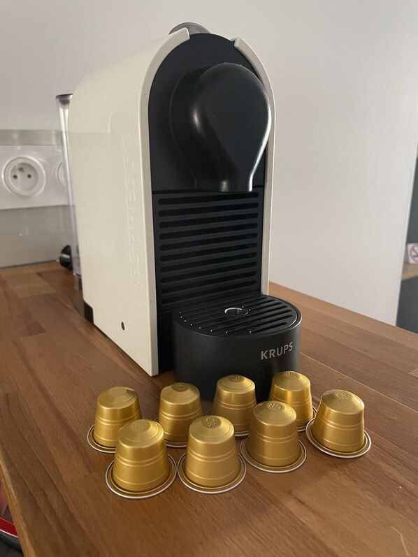 Eine Kaffeemaschine der Marke Krups, eine Steckdose und mehrere goldfarbene Kaffeekapseln auf einem Holztisch.