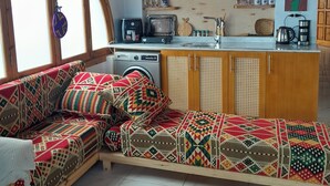 A cozy living room with a sofa, a coffee table, and a kitchen area with a washing machine, a kettle, and a shelf with decorative items. - Tala Boutique Accommodation 14 (Hurghada)