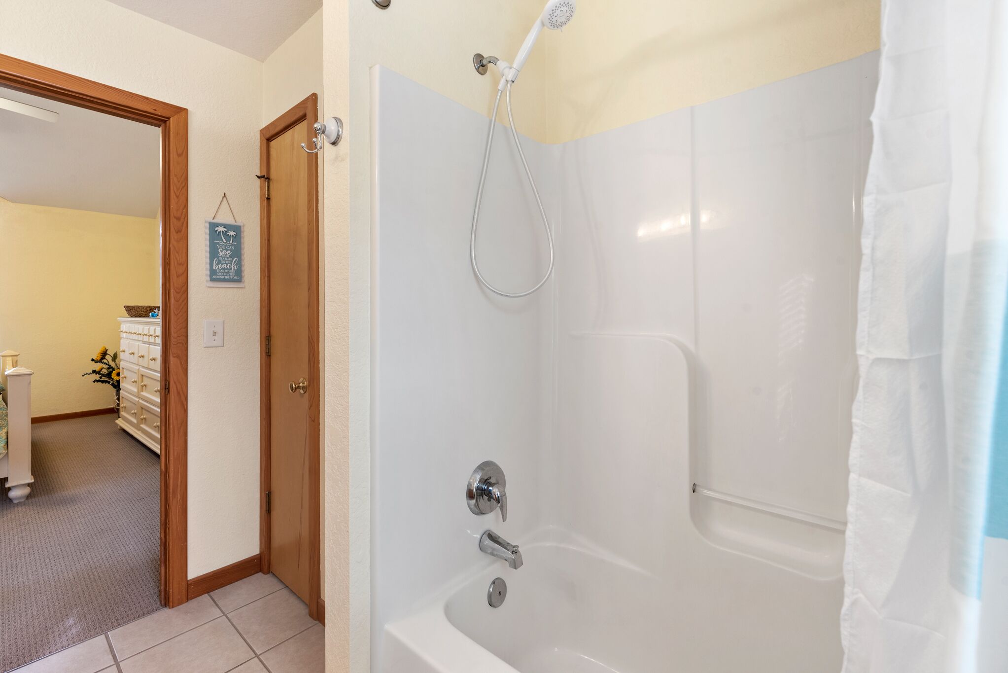 Une salle de bain équipée d’une baignoire, d’une douche et d’une porte en bois donnant sur une autre pièce.