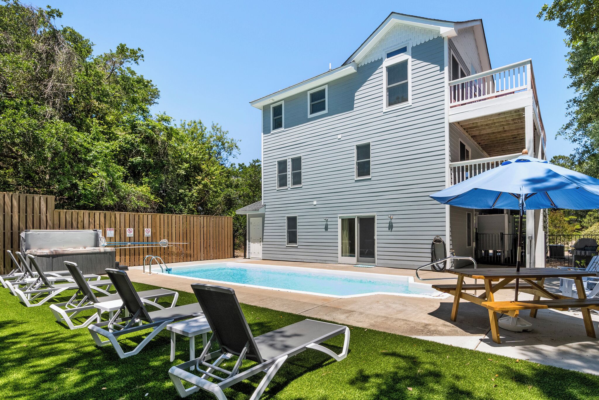 Una casa de dos pisos con piscina, mobiliario exterior y una terraza de madera.