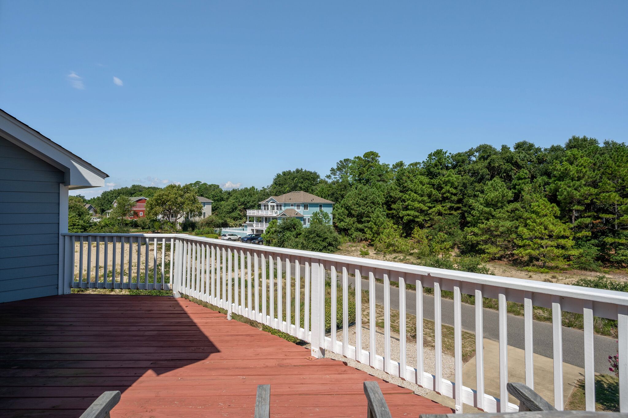 A wooden deck with a white railing, leading to a house with a blue roof and a white fence.