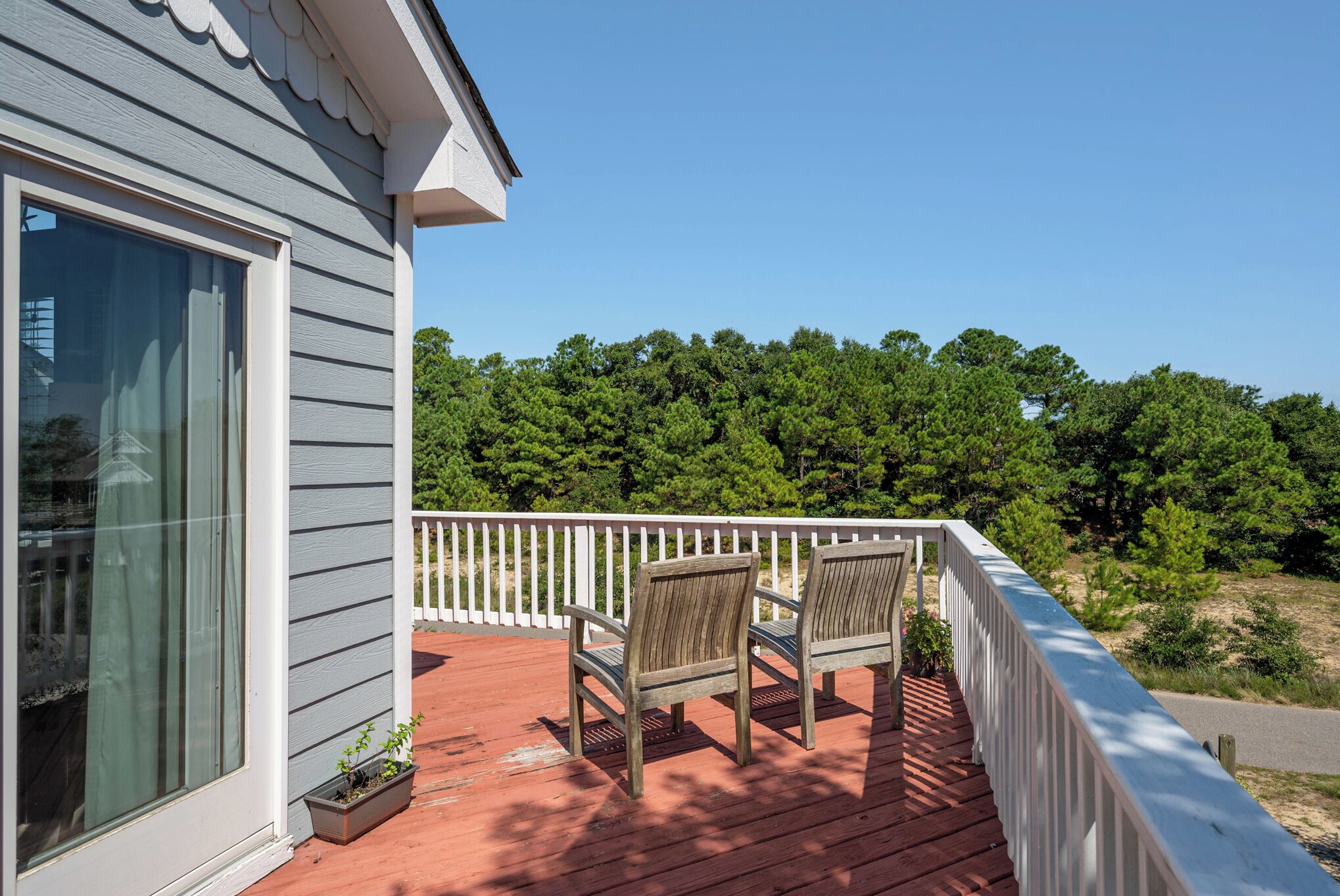 A wooden deck with two chairs and a potted plant, overlooking a forested area.
