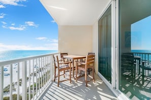 A balcony with a table and chairs, overlooking a beach with umbrellas.