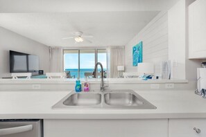 A modern kitchen with a large sink, a ceiling fan, and a view of the ocean through large windows.