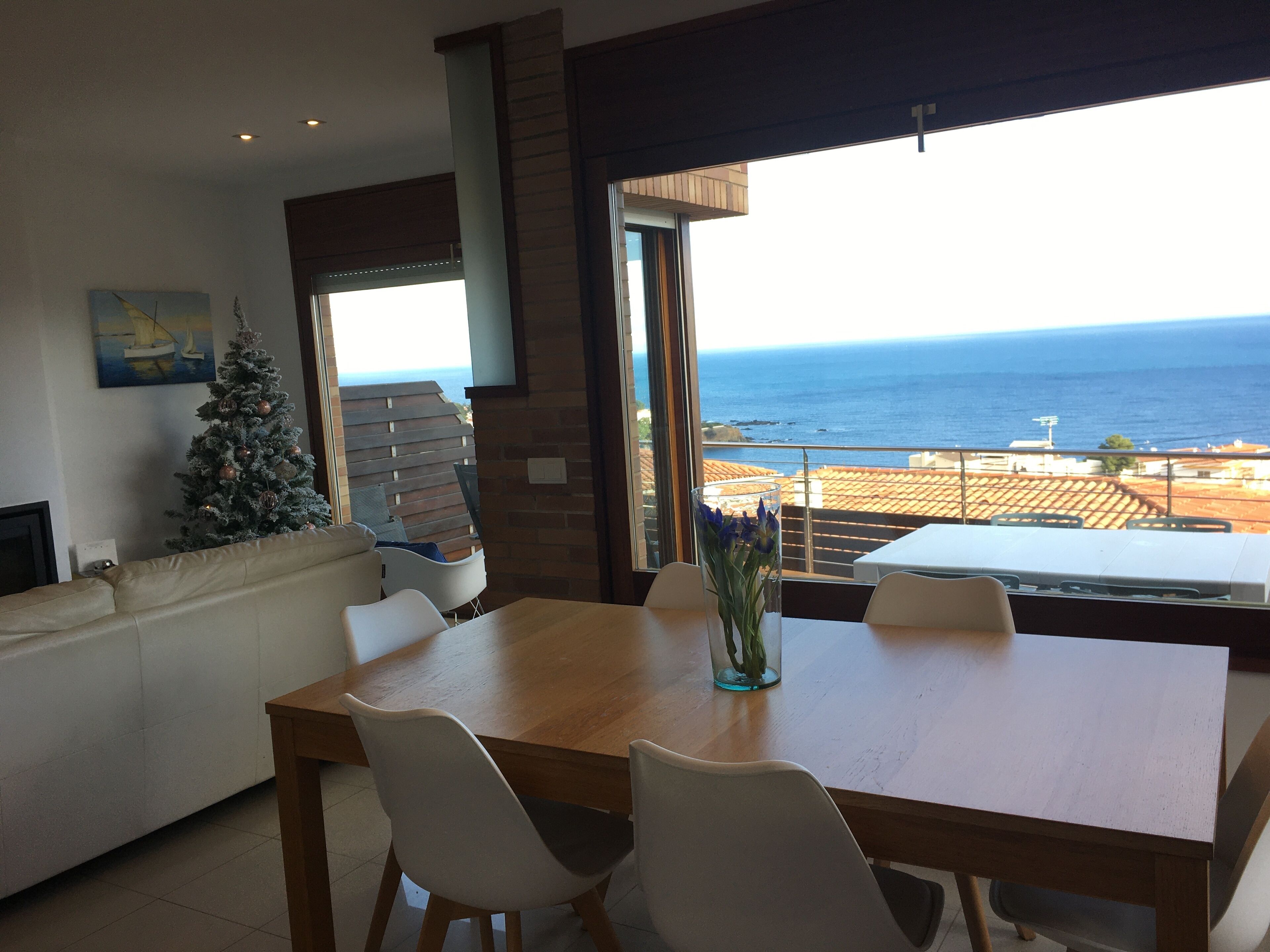 A dining area with a view of the ocean, a Christmas tree, and a fireplace.