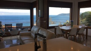 A modern living room with a sofa, dining table, and chairs, overlooking a scenic ocean view. - New apartment, high standing, 180º panoramic view of the sea. (Llançà)