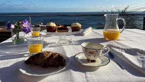 A table set with pastries, a croissant, a jug of orange juice, and a cup, overlooking a scenic ocean view. - New apartment, high standing, 180º panoramic view of the sea. (Llançà)