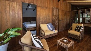 Ein Zimmer mit Holzboden, zwei Korbstühlen, einem kleinen Tisch und einem Bett.