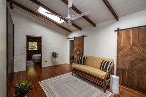 Um quarto com piso de madeira, um sofá, um ventilador de teto, uma porta de celeiro deslizante e um claraboia.