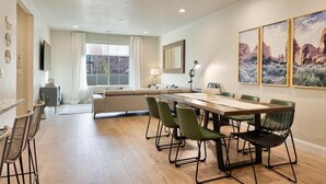 Un salon moderne comprenant un coin repas, un canapé, un téléviseur et une grande fenêtre avec des rideaux.