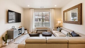 Un salon moderne avec un canapé, une table basse, un téléviseur et une grande fenêtre avec des rideaux.