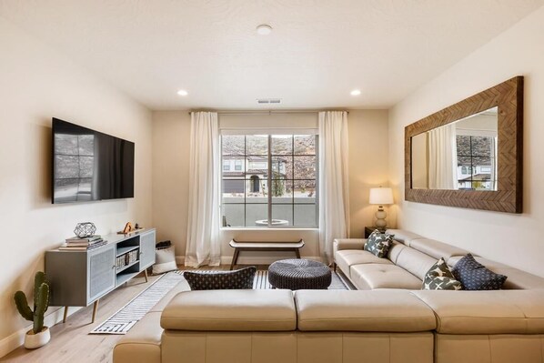 A modern living room with a sofa, a coffee table, a TV, and a large window with curtains. - Angel's Landing: Pickleball, Fire Table, Games, Piano (Washtington)