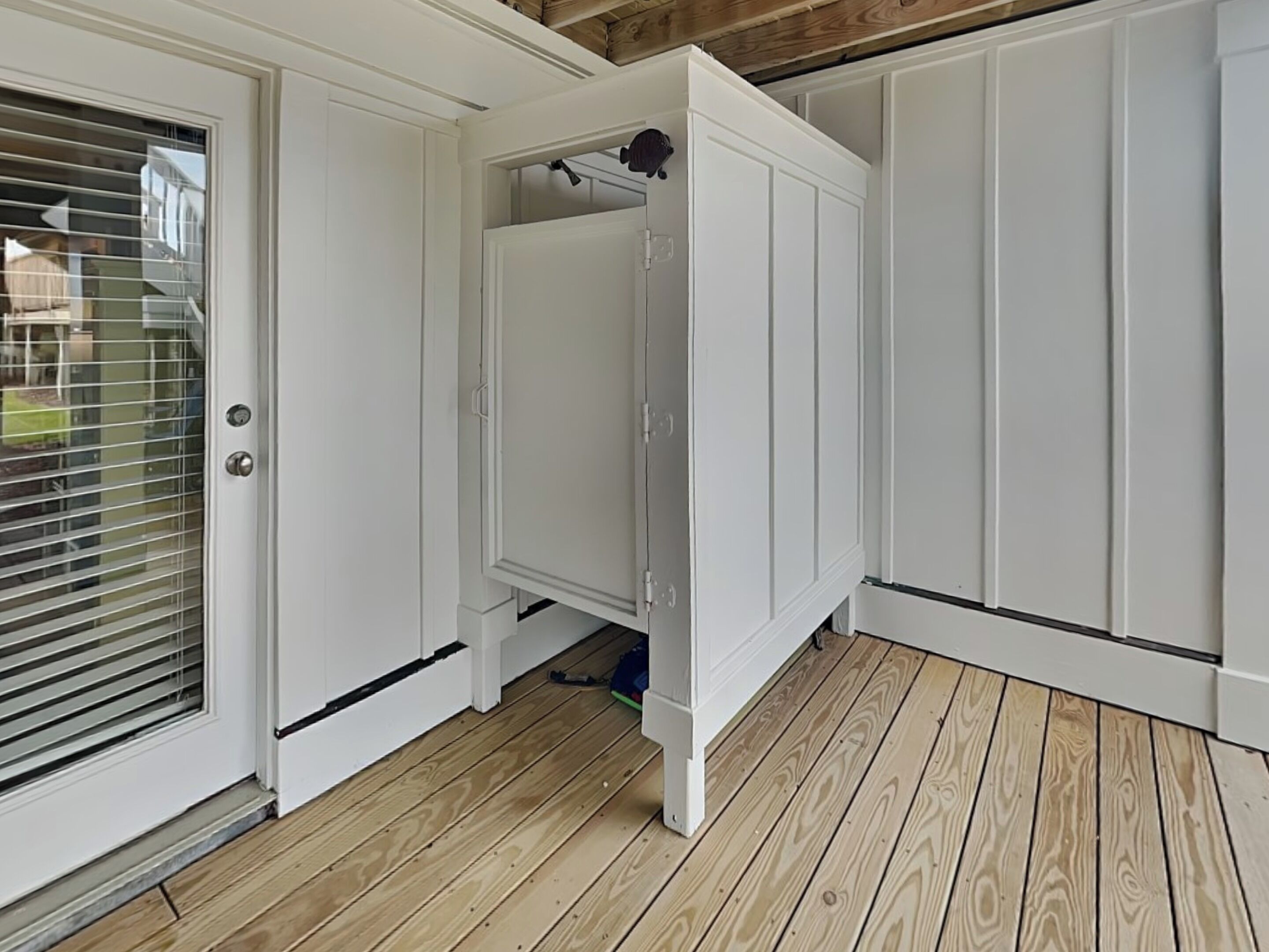 Un placard blanc avec une porte coulissante, un plancher en bois et une petite fenêtre avec des stores.