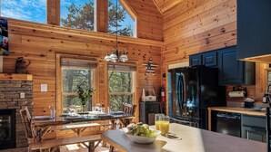 A wooden cabin interior with a dining area, kitchen, and large windows. - Outdoor movie theater, Fire pit, Hot tub, Game rm, 3Mi to Parkway, Pet friendly! (Pigeon Forge)