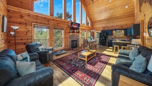 A spacious living room with a fireplace, large windows, and a cozy seating area. - Outdoor movie theater, Fire pit, Hot tub, Game rm, 3Mi to Parkway, Pet friendly! (Pigeon Forge)