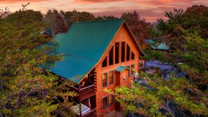 A log cabin with a green roof surrounded by dense trees. - Outdoor movie theater, Fire pit, Hot tub, Game rm, 3Mi to Parkway, Pet friendly! (Pigeon Forge)