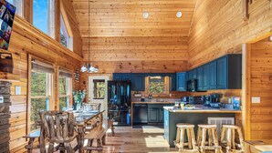 A wooden cabin interior with a dining area, kitchen, and bar stools. - Outdoor movie theater, Fire pit, Hot tub, Game rm, 3Mi to Parkway, Pet friendly! (Pigeon Forge)