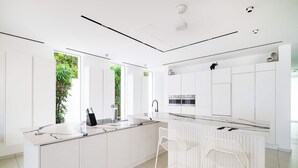 A modern kitchen with white cabinetry, a marble countertop, and a view of greenery outside.