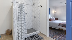 A shower with a hexagonal tile pattern, a bed with a colorful blanket, and a blue door. - Casa del Norte - Secluded Home in Del Norte Mtns (Alpine)
