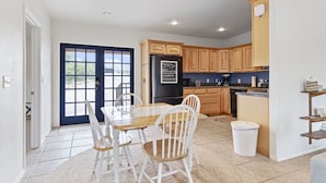 A modern kitchen with wooden cabinets, a black refrigerator, and a dining table with white chairs. - Casa del Norte - Secluded Home in Del Norte Mtns (Alpine)
