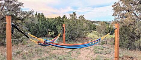 A hammock suspended between wooden posts in a natural setting with trees and shrubs in the background.