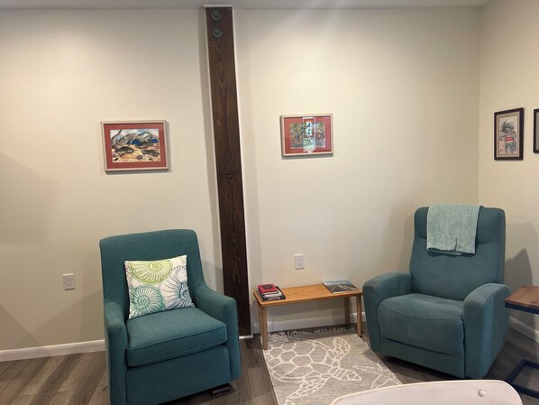 A living room with teal armchairs, a wooden coffee table, and two framed artworks on the walls. - Emerald Mermaid cozy studio apt private beach access including parking & shower (Emerald Isle)