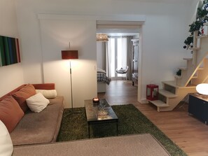 Una sala de estar moderna con un sofá, una mesa de centro y una lámpara de pie. Se observa una escalera que conduce a otro nivel.