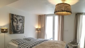 Een slaapkamer met een bed, een stoel, een vloerlamp en een schilderij aan de muur.