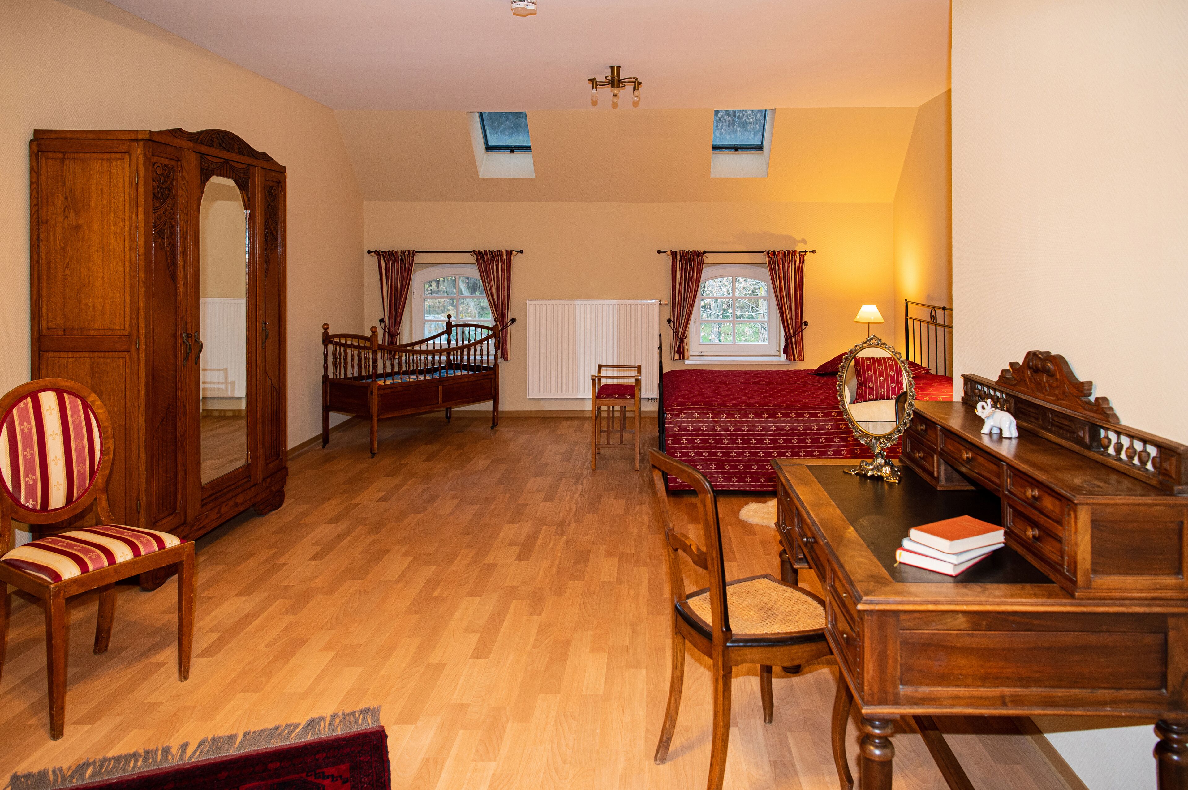 Una habitación con piso de madera, una mesa de comedor con sillas, un espejo grande y dos ventanas con cortinas.