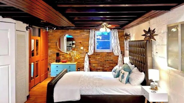 Une chambre à coucher avec un lit, une table de chevet, une fenêtre avec des rideaux, un miroir et une décoration en forme d’étoile sur le mur.