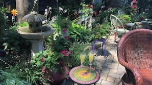 Une terrasse de jardin avec une table en pierre, des plantes en pot, un fauteuil en osier et un abreuvoir à oiseaux.