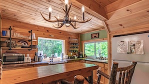 A wooden interior with a kitchen area, a chandelier, and a refrigerator. - Cabin close to town, private beach, parking & hot tub (Old Forge)