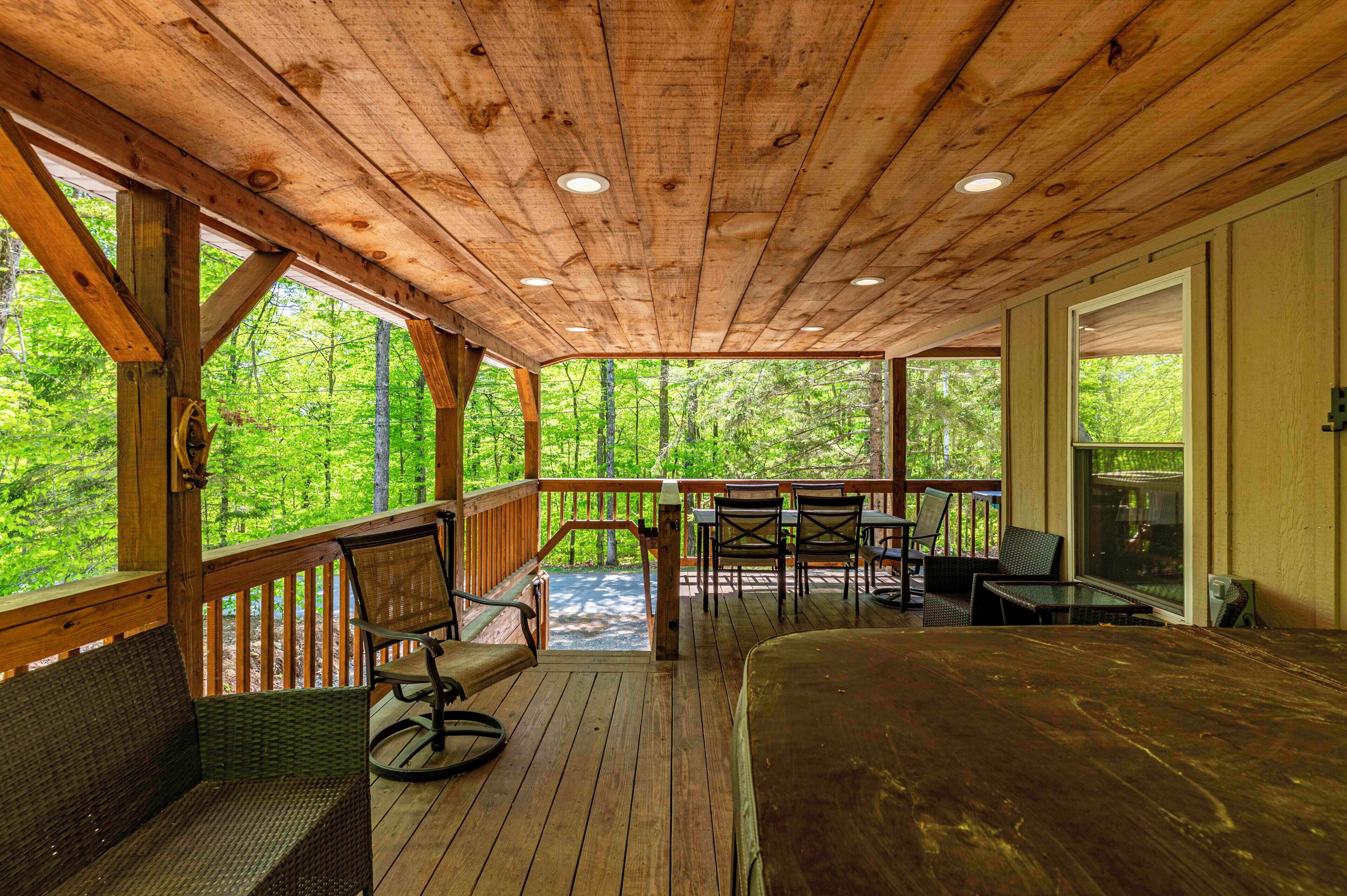 A wooden deck with outdoor seating, a view of the forest, and a large window.