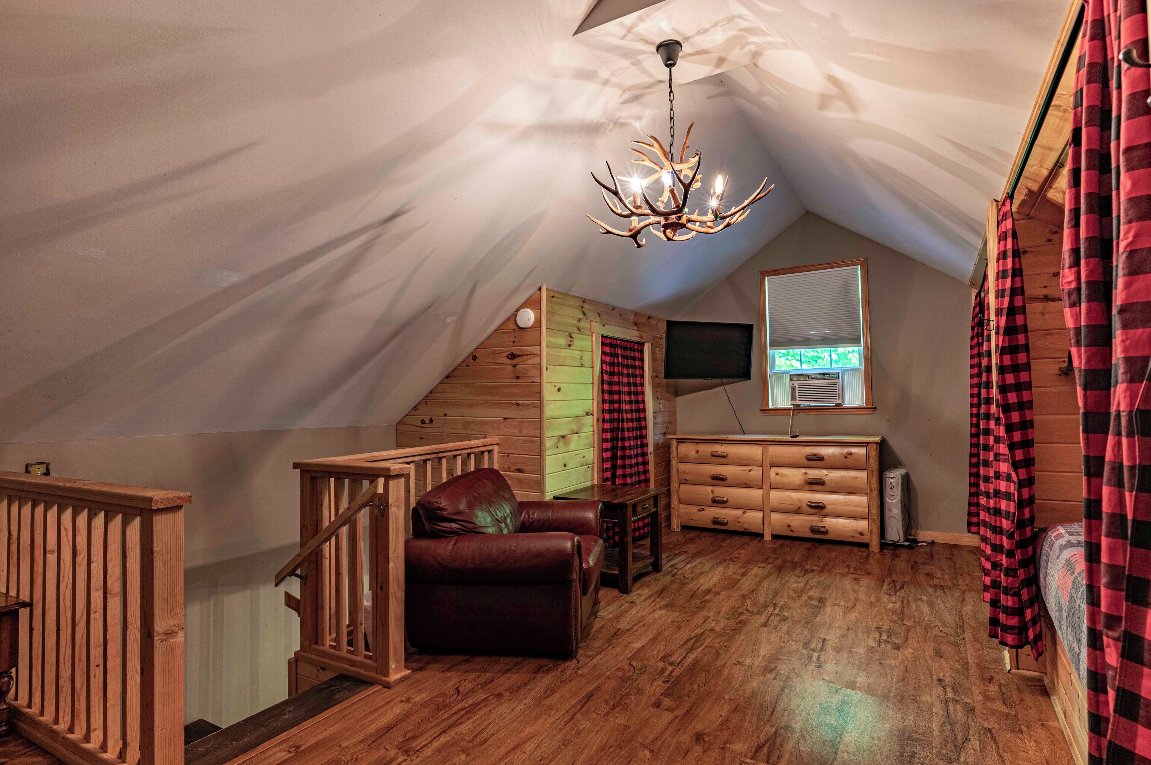 Une chambre confortable située dans les combles, avec un plafond en bois, un lustre, un canapé en cuir, une commode et des rideaux à carreaux.