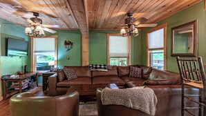A cozy living room with a brown leather couch, wooden ceiling, and two ceiling fans. - Cabin close to town, private beach, parking & hot tub (Old Forge)
