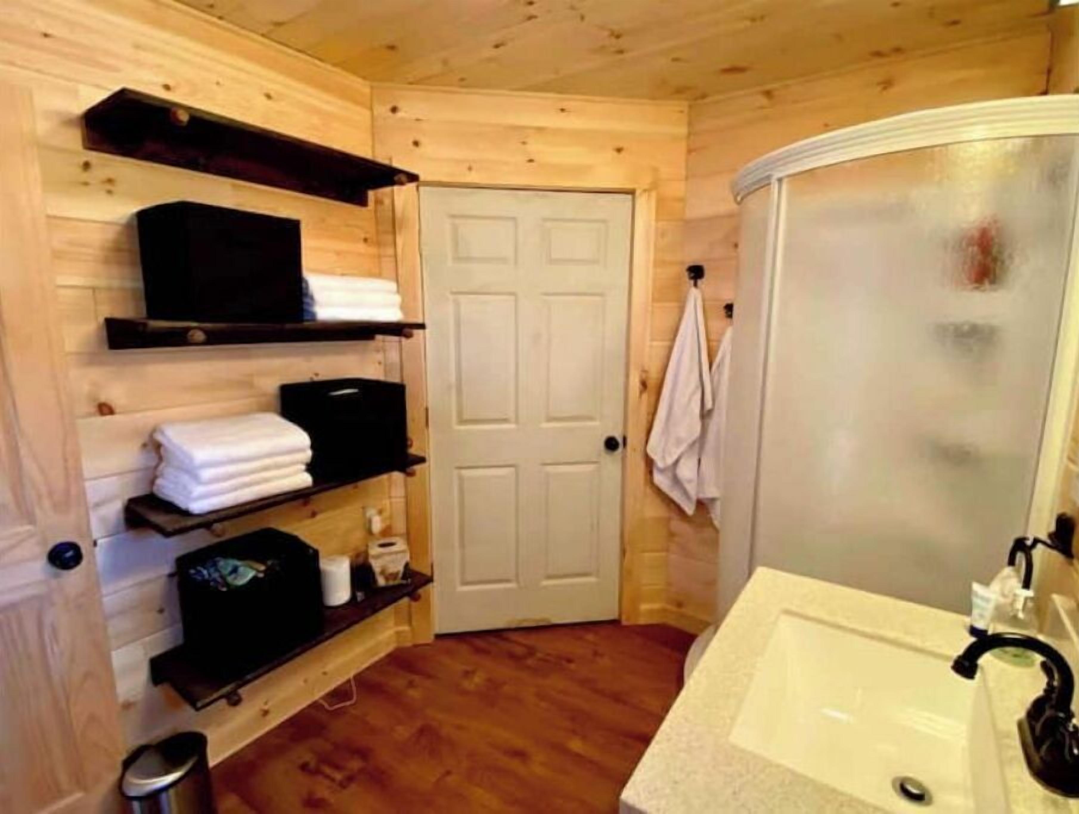 Ett badrum med träpanel på väggarna, en vit dörr, ett handfat och hyllor med handdukar.