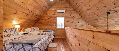 Ein gemütliches Schlafzimmer im Dachgeschoss mit Holzwänden, einer geneigten Decke, einem Deckenventilator, einem Fenster und einem Bett mit Karo-Bettwäsche.