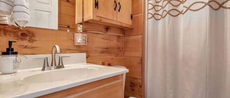 Un baño estilo cabaña de madera con un lavamanos blanco, un inodoro y una cortina de ducha con un diseño geométrico.