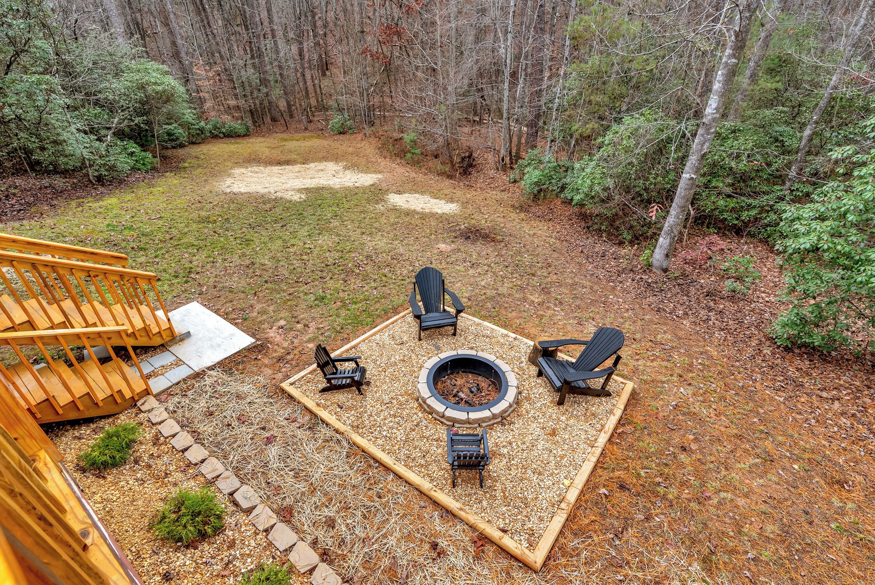 Um quintal com lareira, quatro cadeiras Adirondack e um deck de madeira.