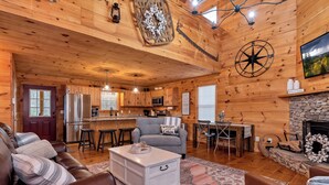 Un interior de cabaña acogedor, con paredes de madera, una chimenea, un comedor y una cocina equipada con electrodomésticos modernos.