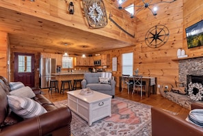 Cozy cabin interior with a central living area, kitchen, dining space, and stone fireplace.
