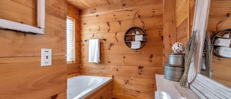 A wooden cabin bathroom with a bathtub, a towel rack, and a mirror.