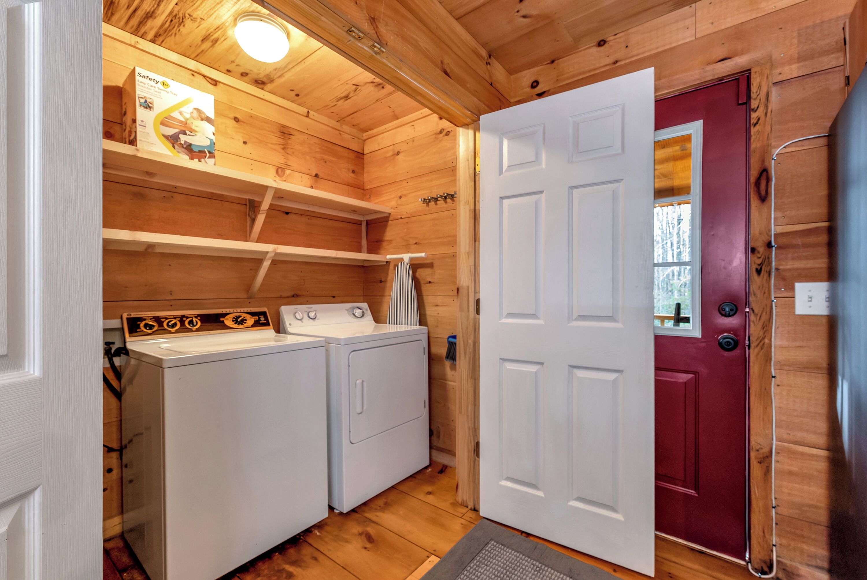 A laundry room with two white washers and dryers, wooden walls, a red door, and a safety sign on the wall.