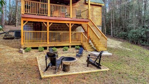 Una cabaña de madera de dos pisos con terraza, mobiliario exterior y un brasero.
