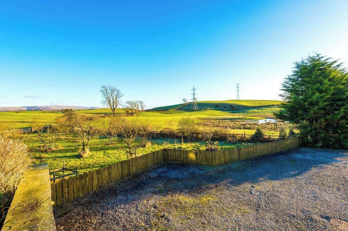 A rural landscape with a wooden fence, a gravel path, and a hill with power lines in the background.