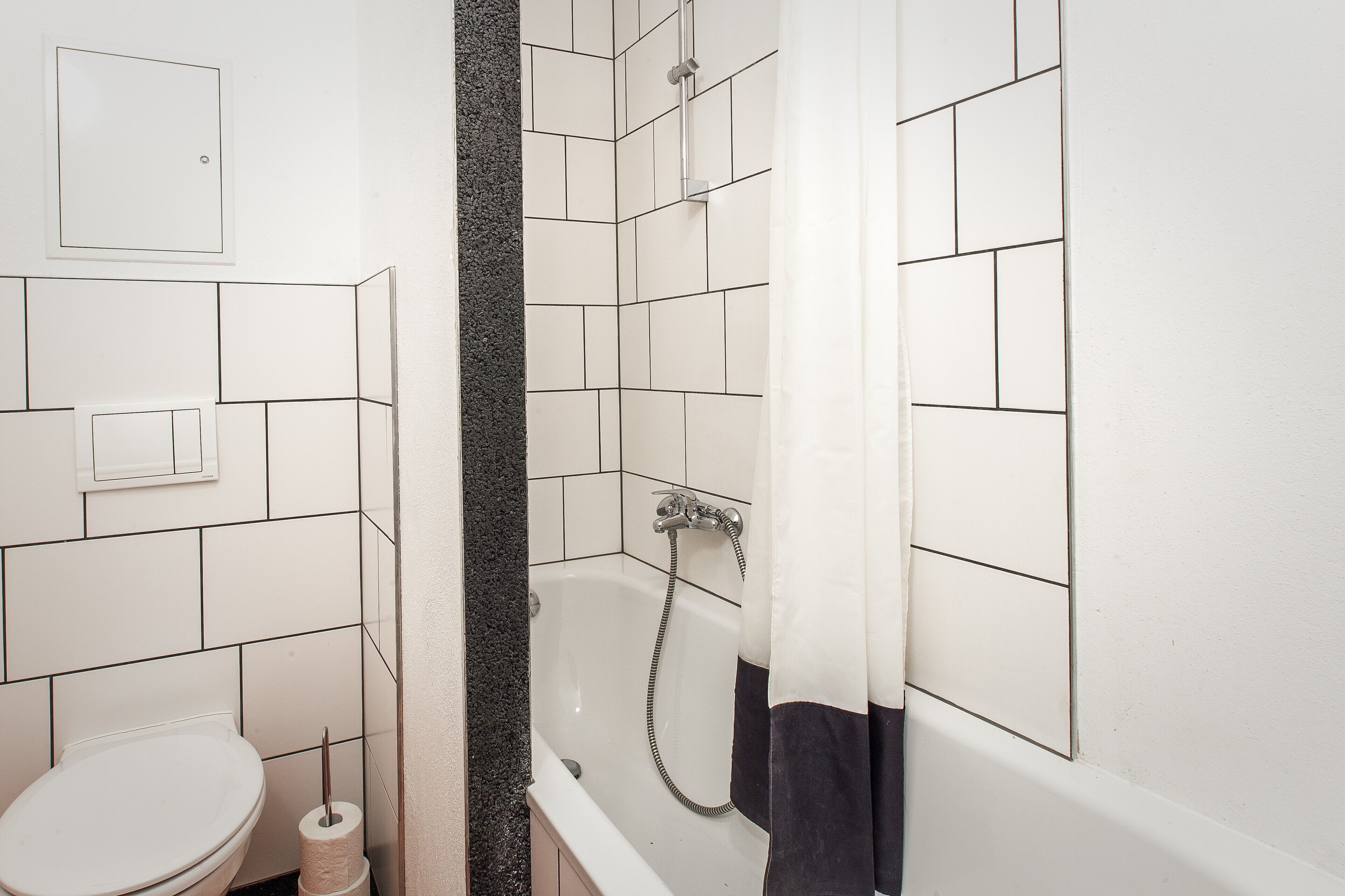 A bathroom with white tiles, a bathtub, a toilet, and a shower curtain.