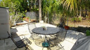 A patio with a round metal table and chairs, surrounded by a chain-link fence and various plants. - Venture Out #79 Gulf Loop Comes With Golf Cart!!! (Panama City)