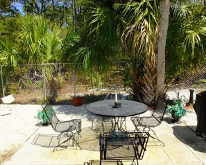 Eine Terrassengruppe im Freien mit rundem Tisch und Stühlen, umgeben von Pflanzen und einem Zaun.
