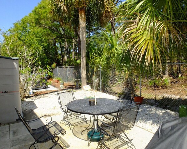 Relax in the serene patio area surrounded by lush greenery and a palm tree, complete with a round table and four chairs.