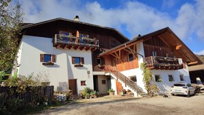 A two-story wooden chalet with balconies, a gravel driveway, and a parked car. - Farm❤ (Eppan)